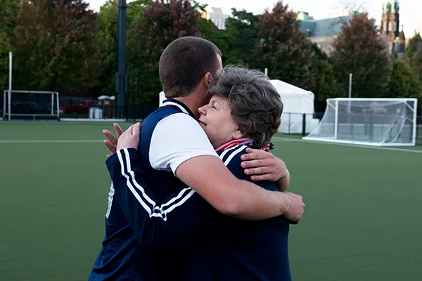An older woman hugs a young man wearing a soccer uniform