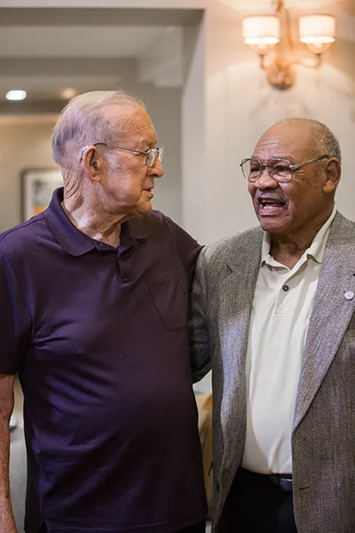 Two older men chatting with each other while standing up indoors.