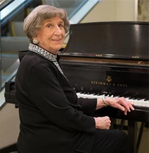 A well-dressed woman smiles at the camera while sitting at the piano.