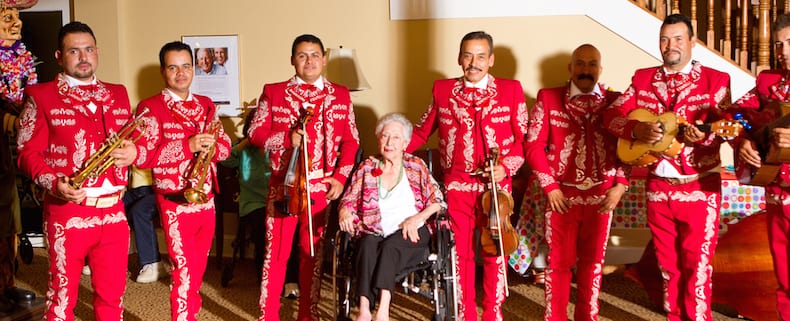 A mariachi band wearing red outfits surround an older woman sitting in a chair