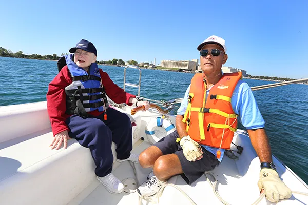 An older woman steers a sailboat while a man looks on.