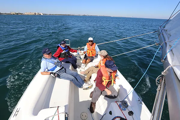 A group of people sit at the back of a small sailboat
