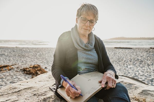Wish recipient Colleen writes poetry by hand in a notebook while sitting on the beach