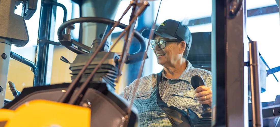 An older woman smiles while driving a bulldozer.