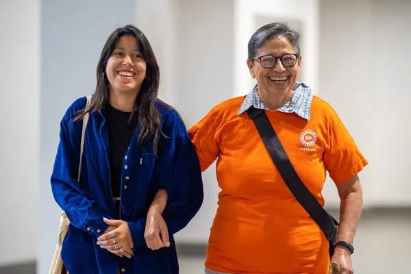 An older and younger Chicana woman stand together, linking arms.