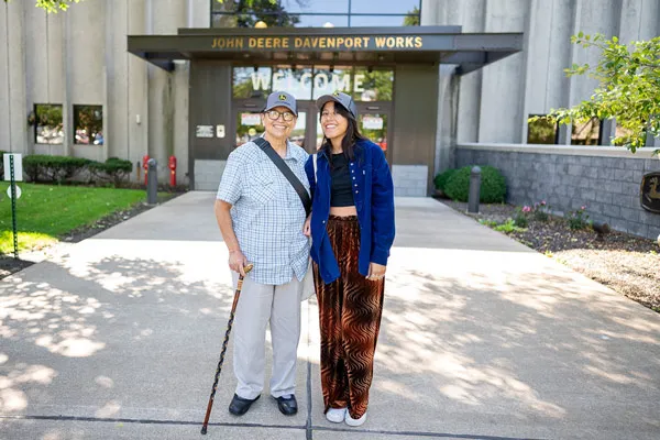 A woman with a cane stands with a younger woman outside of a building.