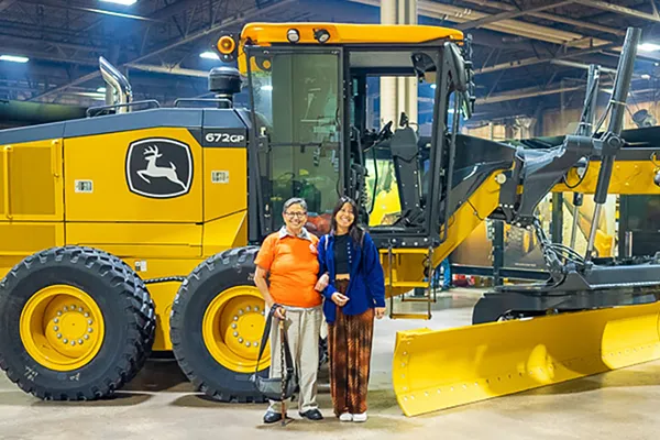 Two women stand next to a bulldozer.