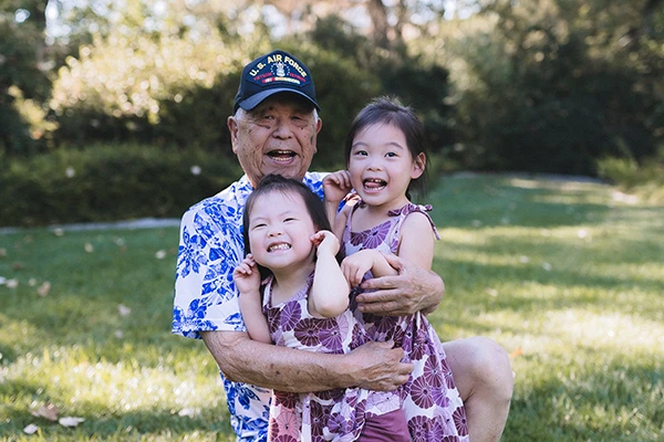 An older man holds his two young granddaughters in the park