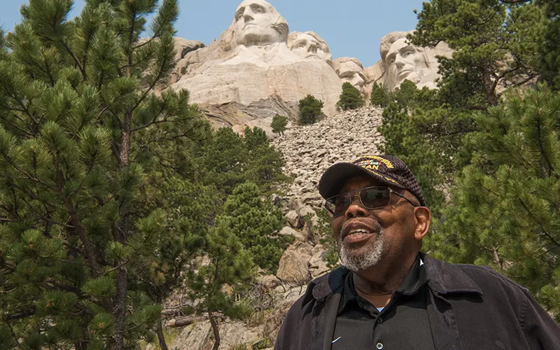 An older African-American man stands in front of Mt Rushmore