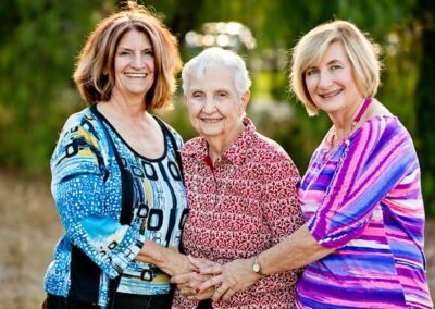 Three women smile at the camera, the two younger women have their arms around the older woman.
