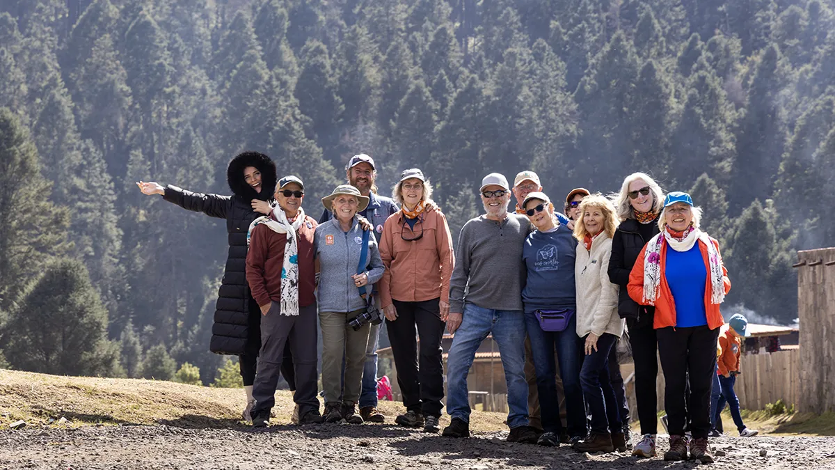 A hiking tour group stands near a mountain forest.