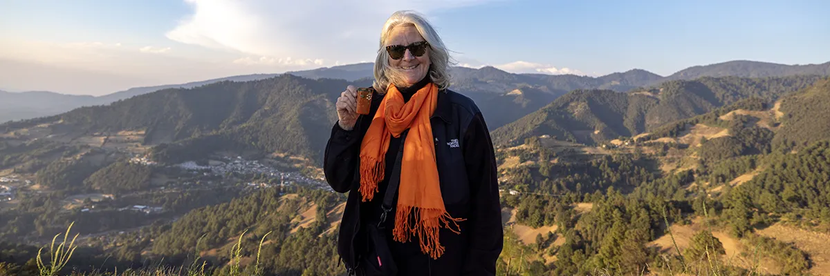 An older woman with an orange scarf hikes mountains in Mexico.