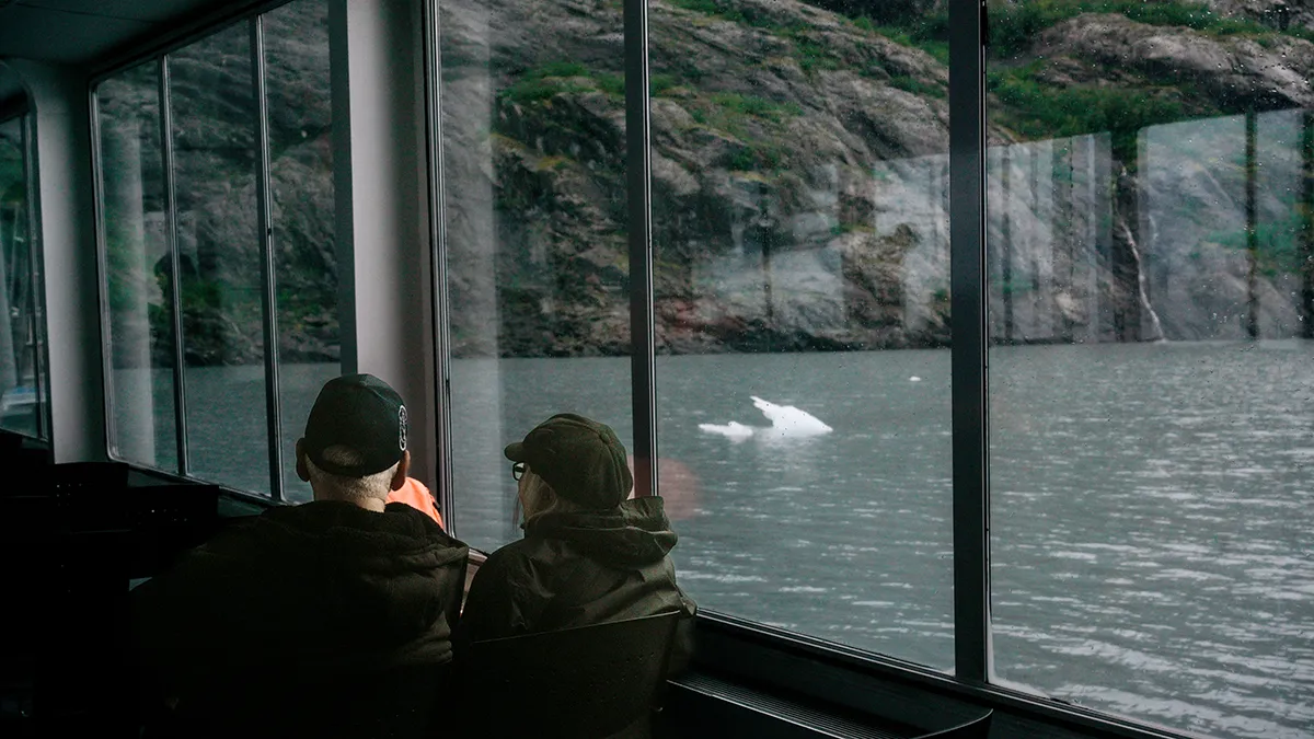 Two people watch for whales out of a boat window.