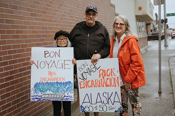Older adults hold handmade goodbye signs before a trip.