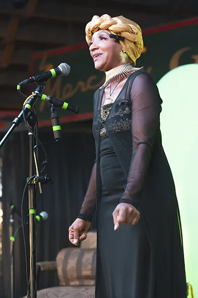 A Black woman sings into a microphone on stage.