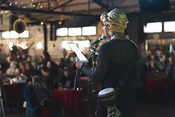 A woman stands in front of a live audience.