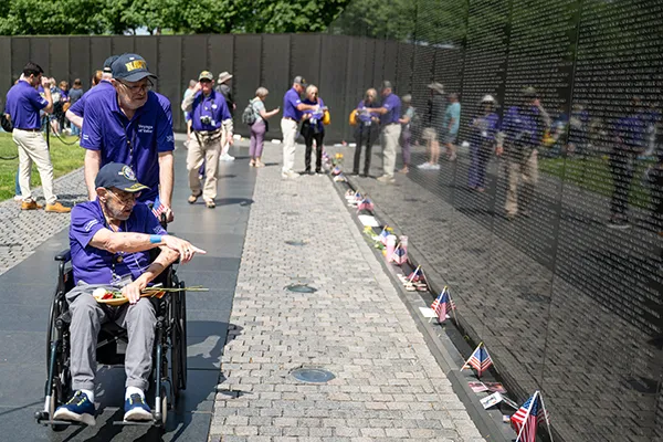 A man in a wheelchair points at a name on the Vietnam Veterans Memorial Wall.