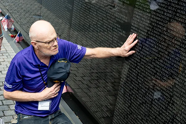 A man removes his hat while touching the Vietnam Veterans Memorial Wall.