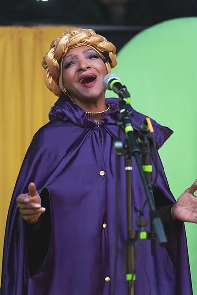 An older African American woman sings into a microphone.