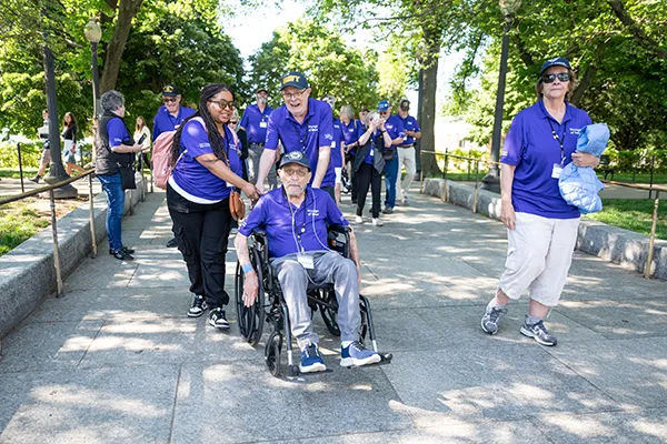 An older man and young woman push another man in a wheelchair.