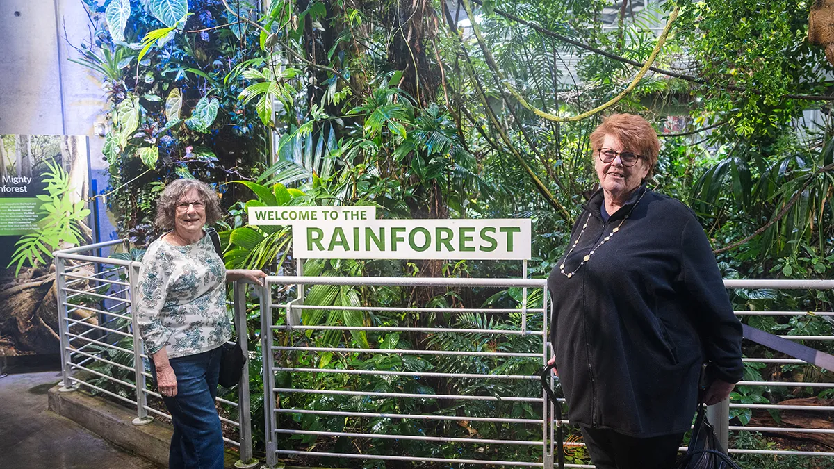 Two women stand in front of the sign for an indoor rainforest exhibit.