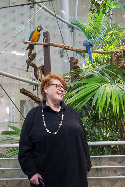 A woman smiles in front of a blue and yellow macaw.