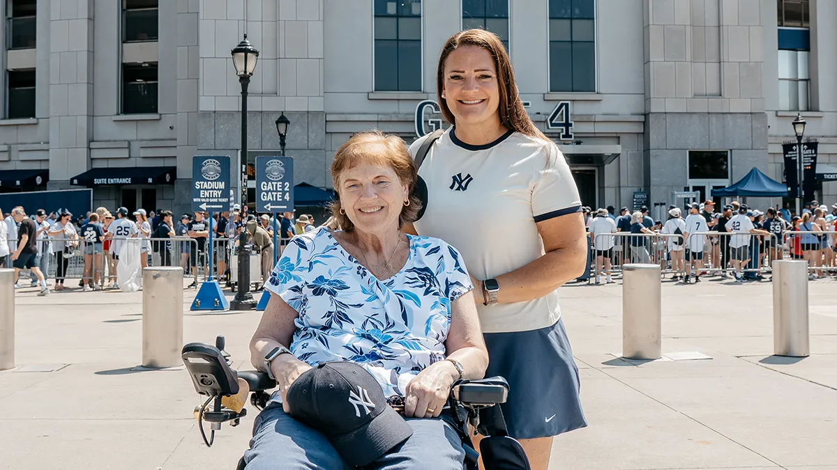 A young woman in New York Yankees gear stands behind an older woman in a wheelchair.
