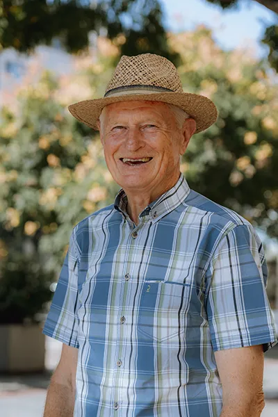 An older gentleman wearing a straw hat smiles.