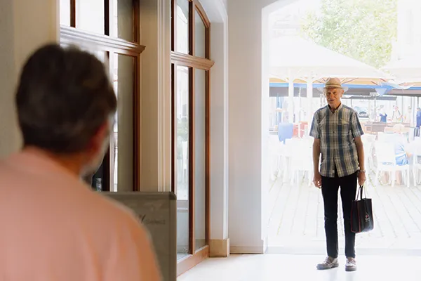 A man with a bag stands in a doorway facing a woman.