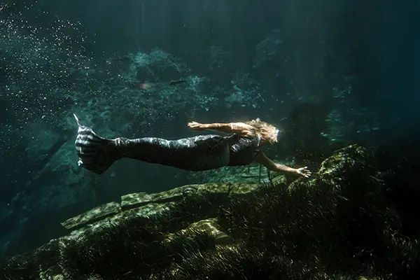 A woman swims underwater wearing a mermaid tail.