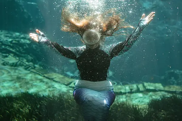 : A woman in a dive mask sits on the floor of an underwater cavern.