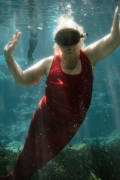 An older woman in a dive mask swims underwater.