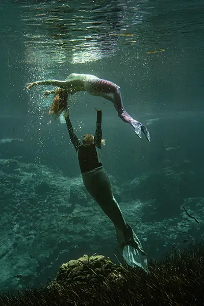 Two women perform an underwater show in mermaid costumes.