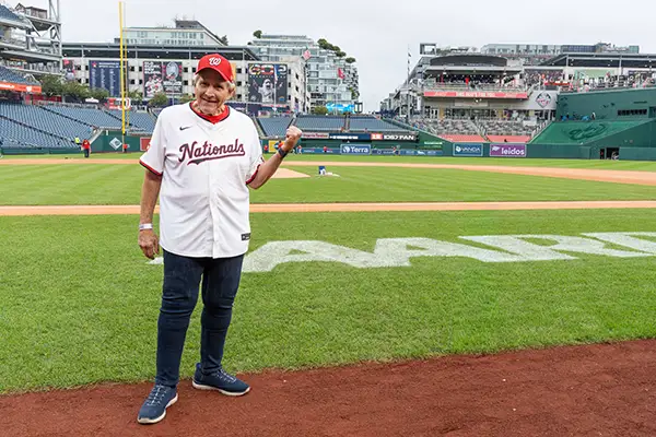 A man stands on a baseball field with the AARP logo painted onto the grass.