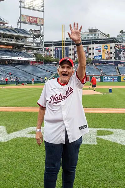 An older man in a Washington Nationals jersey waves from the baseball field.