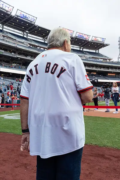 A man in a bat boy jersey looks out on a baseball field.