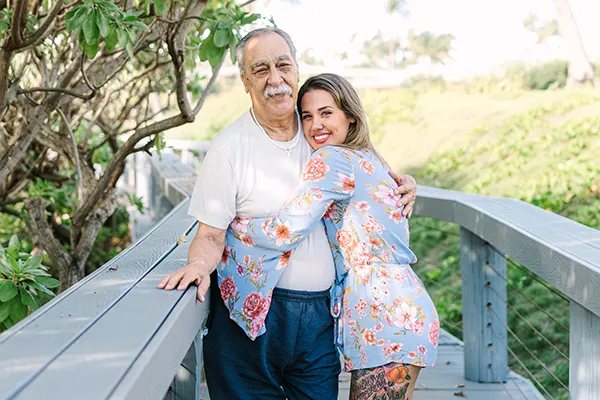A younger woman hugs an older man on a bridge.