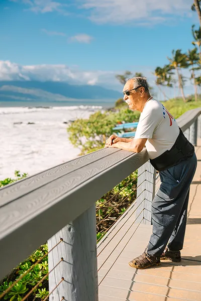 An older man looks out on an ocean shoreline from a scenic walkway.