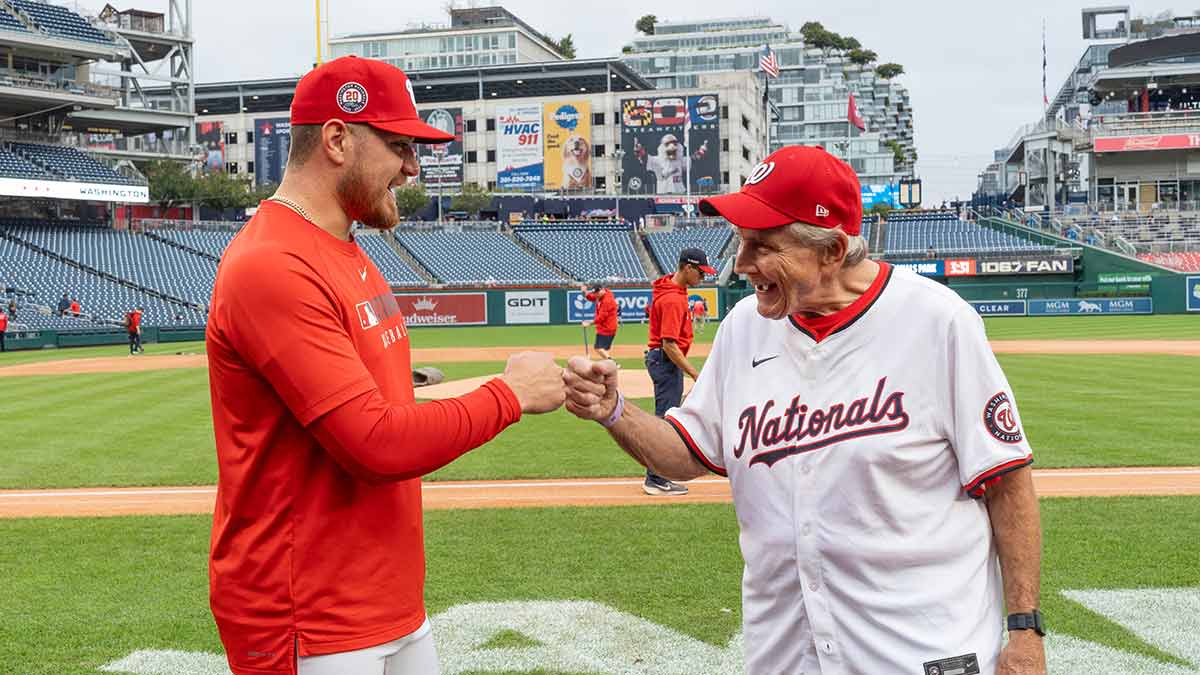 A baseball player fist bumps and older man in a Nationals baseball jersey.