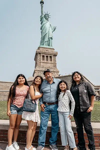 An older man stands with four girls at the Statue of Liberty.
