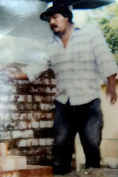 A man stands next to a brick wall in a vintage photograph.