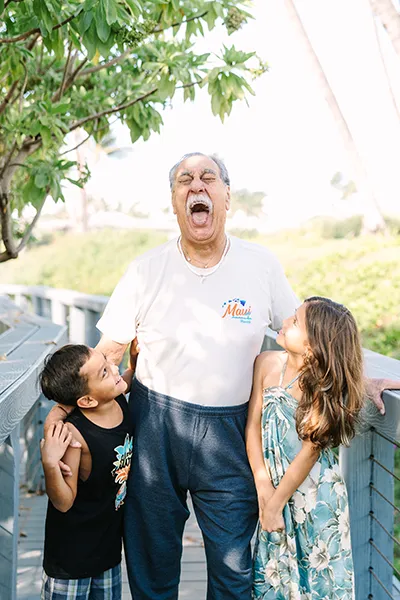 An older man laughs with two young children standing next to him.