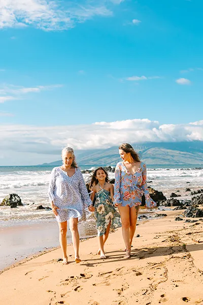 Two women and a girl walk along the beach holding hands.