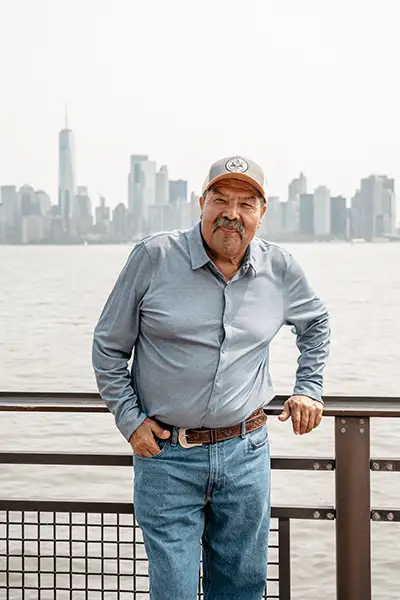 An older Mexican man stands along the water near the city.