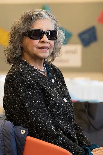 An older woman in sunglasses sits indoors
