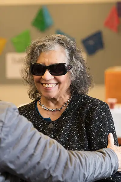 Someone touches the arm of a woman wearing dark glasses