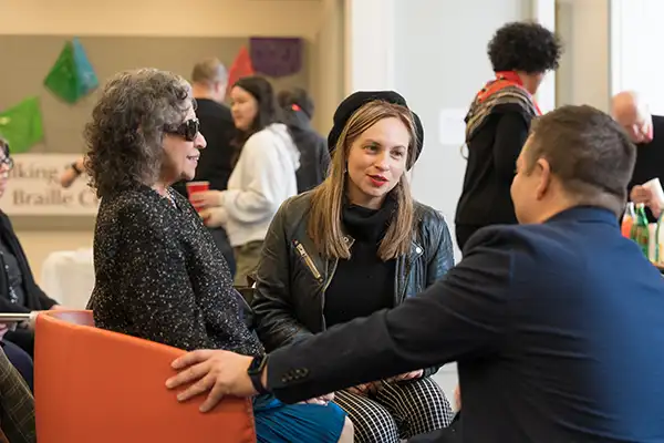 Two women talk with a man while sitting indoors