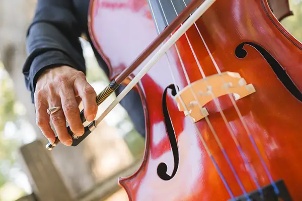 An older woman’s hand holds a bow while playing a cello.