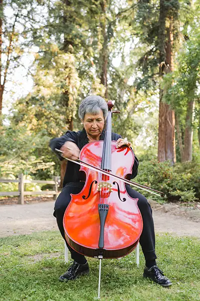 A woman sits while playing a cello outdoors.