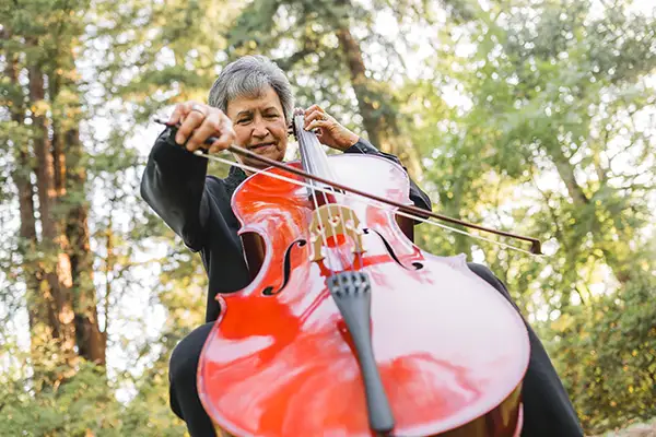 An older Hispanic woman plays a cello outdoors.